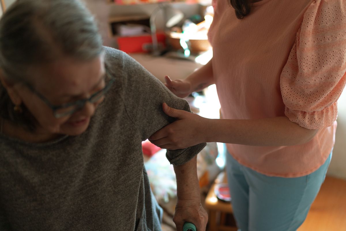 Caregiver thoughtfully assisting an older person at home
